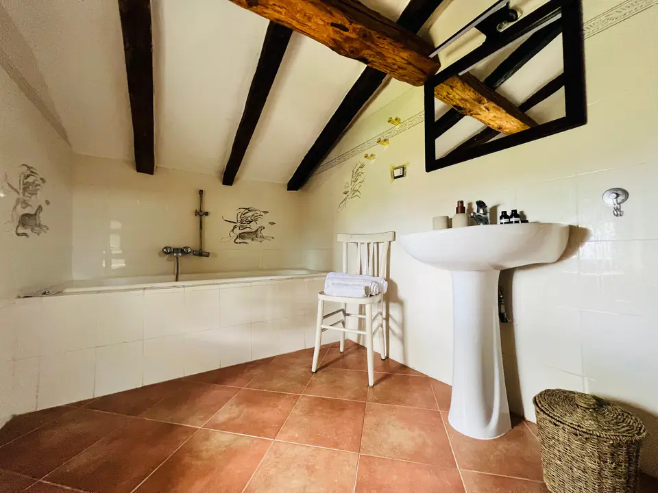 Secondo bagno di Casa Vedetta con vasca da bagno, lavabo bianco e travi a vista