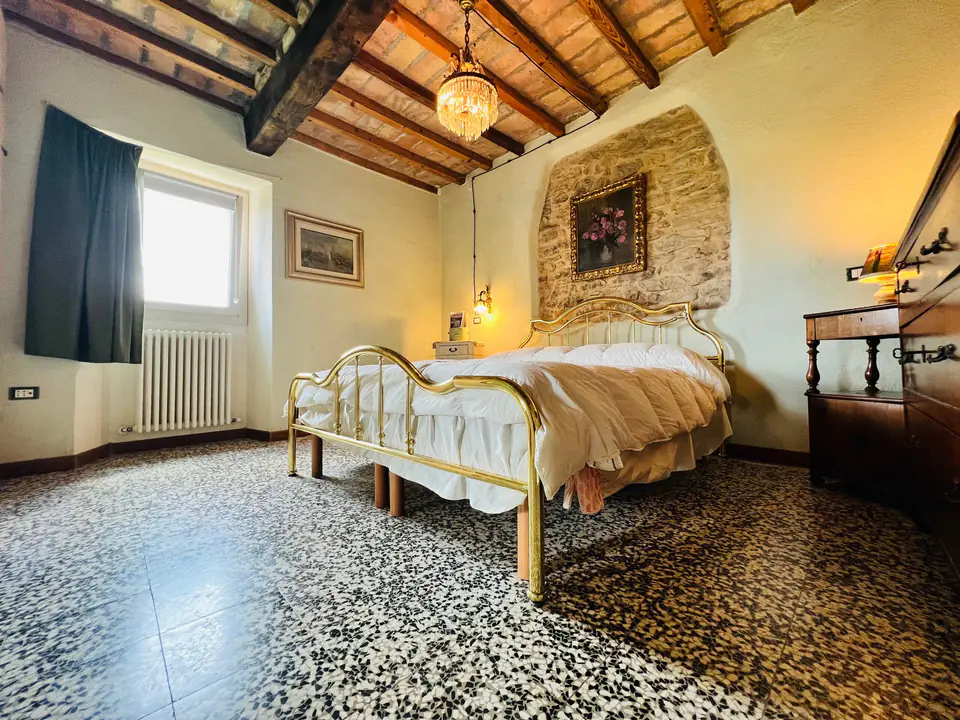 Camera matrimoniale di Casa Vedetta con letto in ferro battuto, travi a vista e parete in pietra
