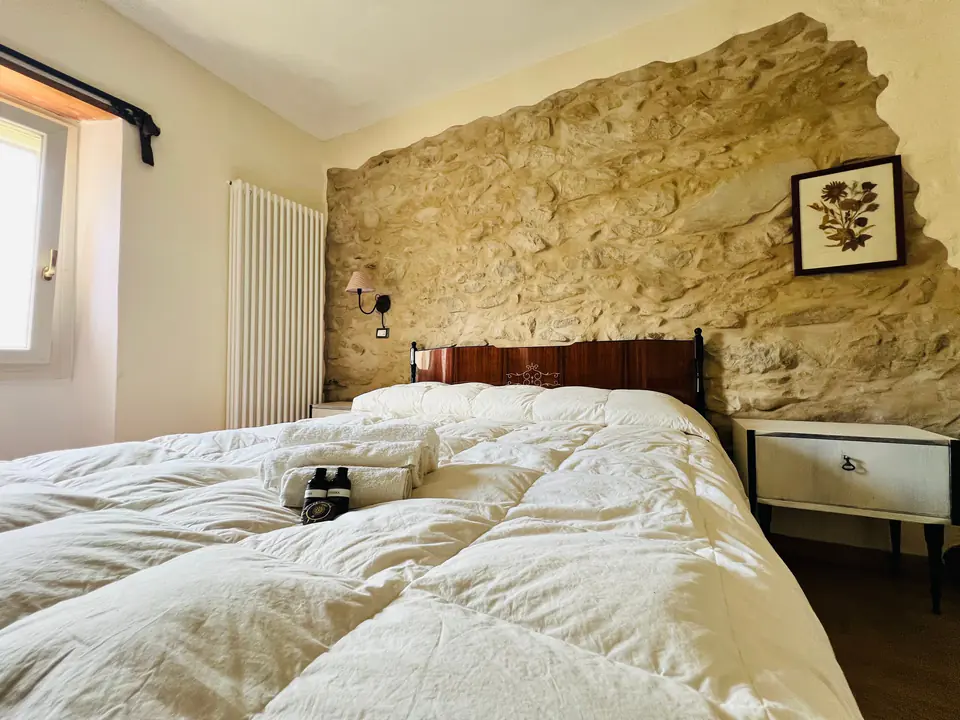 Letto matrimoniale accostato alla parete in pietra naturale di Casa Vedetta