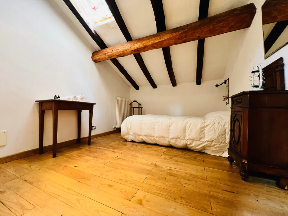 Camera con letto singolo e consolle in legno sotto le travi di Casa Vedetta