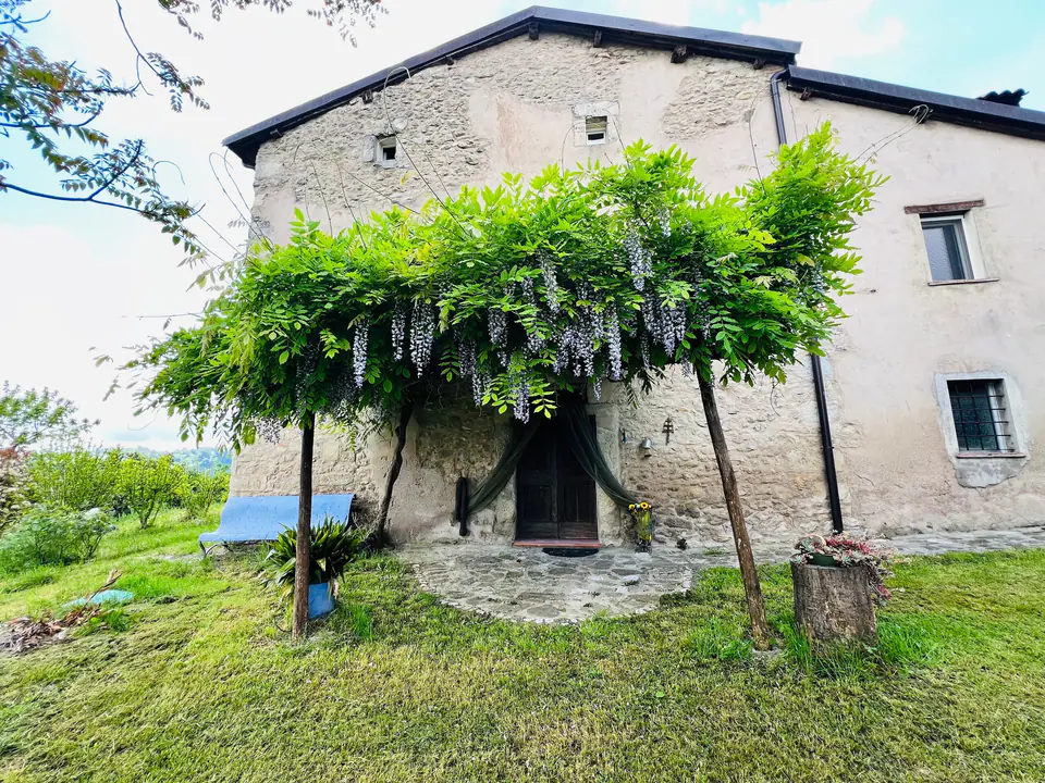 Facciata in pietra di Casa Vedetta con il glicine in fiore e le colline sullo sfondo